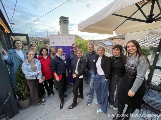 Viele Menschen stehen vor dem Roll-Up der Hannah-Arendt-Initiative unter einem Sonnenschirm und lächeln in die Kamera.